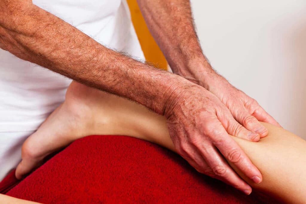 Therapist massaging a patient’s lower leg, hands pressing along the calf on a red blanket.