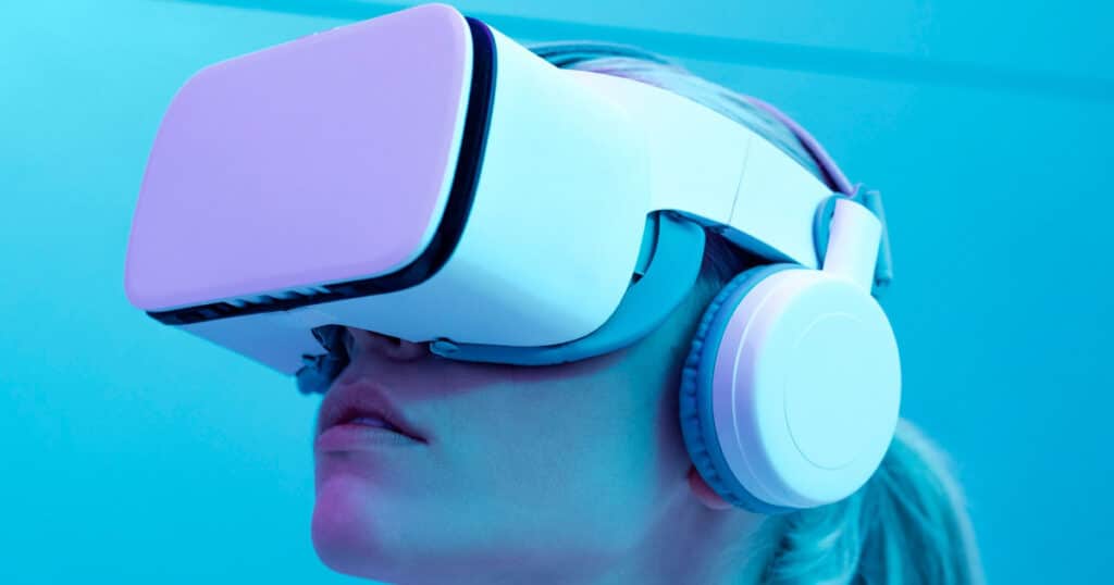 Person wearing a white virtual reality headset and large over-ear headphones against a blue background, immersed in VR experience.
