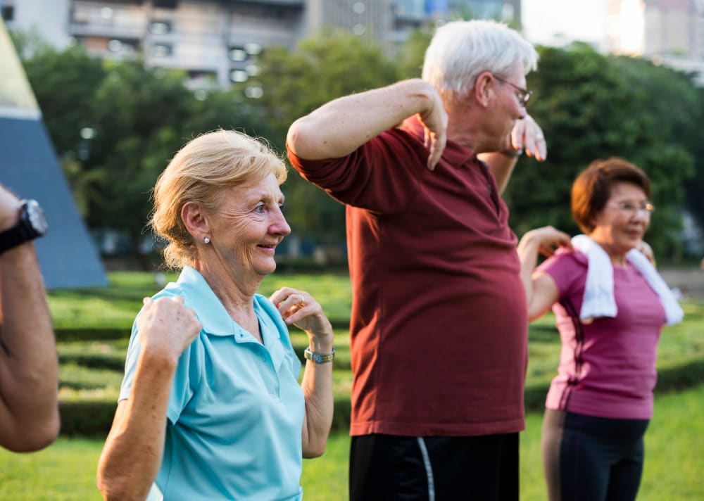 Three seniors outdoors doing arm stretches in a sunny park.