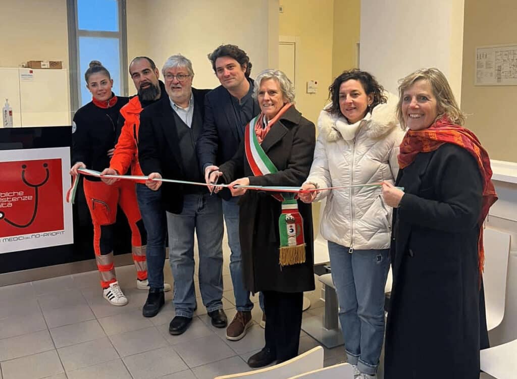 Ribbon-cutting ceremony with eight people holding a red-and-white ribbon inside a clinic or hospital lobby.