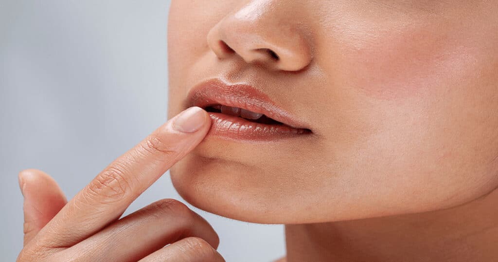 Close-up of a person touching their lips with a finger, showing glossy lips and smooth skin.