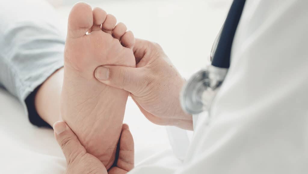 Doctor gently holds a baby's foot for a medical checkup, with a stethoscope visible on the doctor nearby.