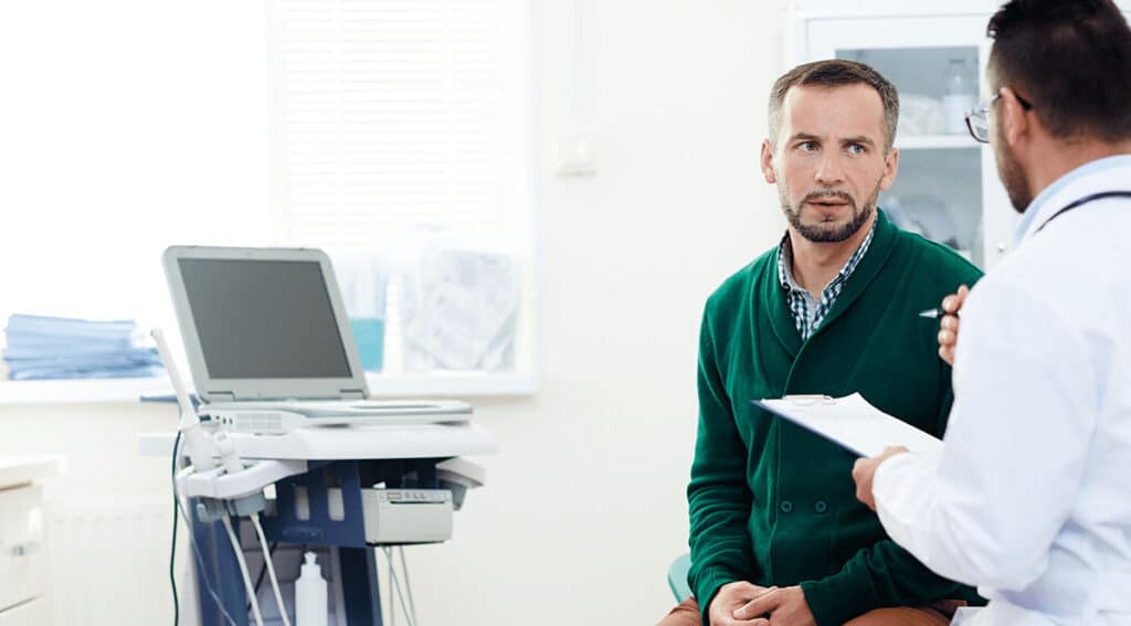 Doctor consults with a patient in a bright clinic, clipboard in hand near medical equipment and an ultrasound machine nearby.