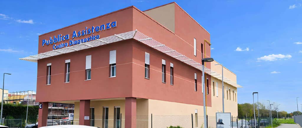 Public health and diagnostic center building with a blue sign reading 'Pubblica Assistenza Centro Diagnostico' against a clear sky, red-brown exterior and white awning.